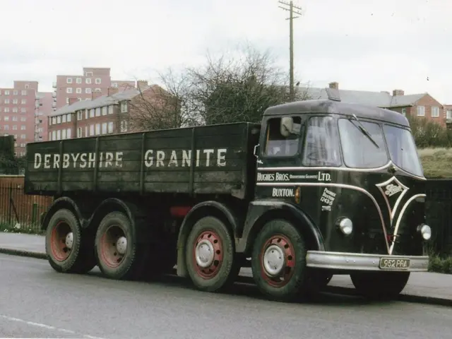 In this image there is a truck on the road. Beside there is a pavement. Behind the fence there are...